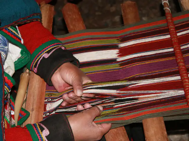 Hands weaving red, purple and white stripes on a traditional backstrap loom in Cusco
