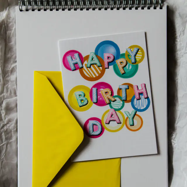 A colorful Happy Birthday card and a bright yellow envelope resting on a spiral sketchbook