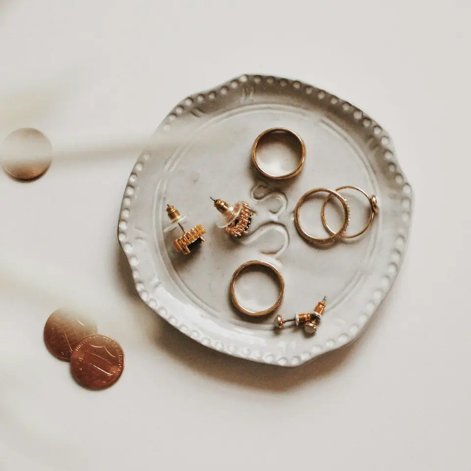 Gold rings and earrings resting in a small ceramic trinket dish with a beaded rim