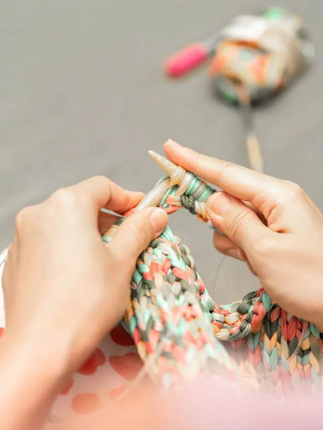 Close-up of hands knitting a piece of chunky multicolor fabric on a pair of needles