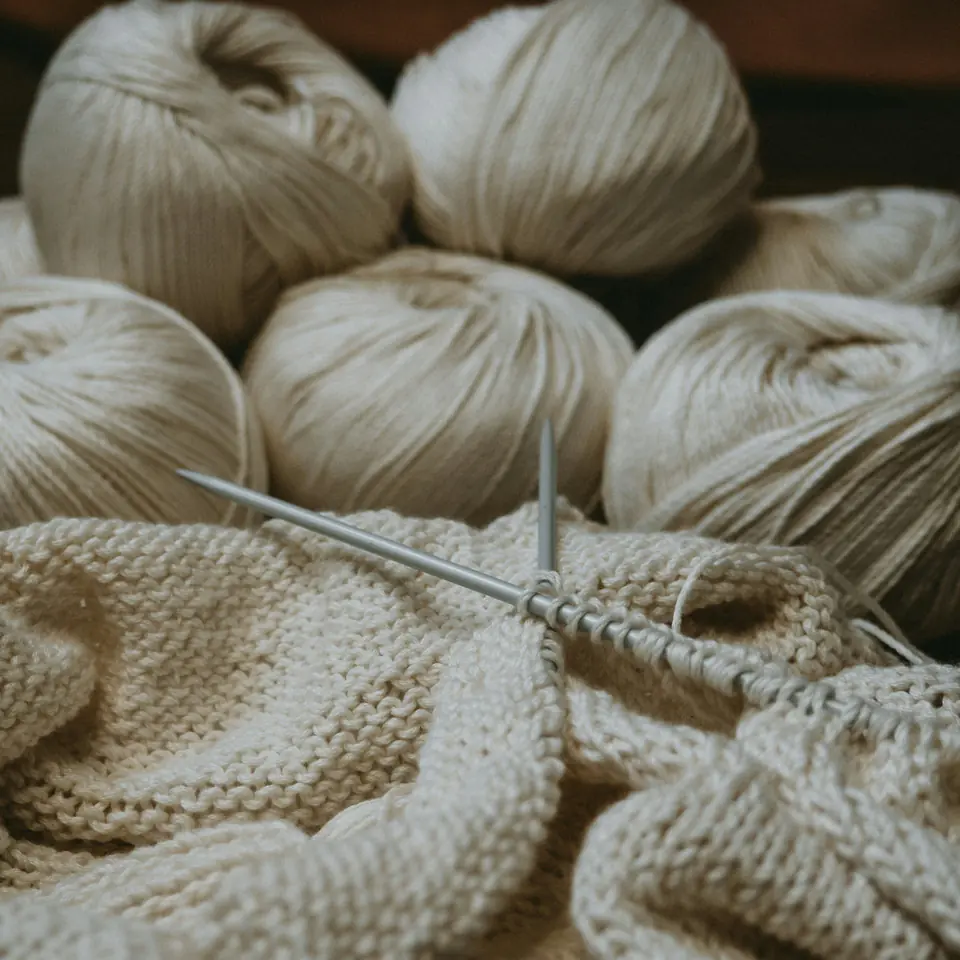 Balls of cream cotton yarn behind a half-knitted panel on metal needles