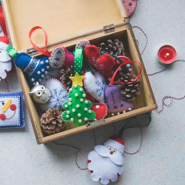 A wooden box of hand-sewn felt Christmas ornaments, from hearts and mittens to a beaded tree, beside a felt Santa
