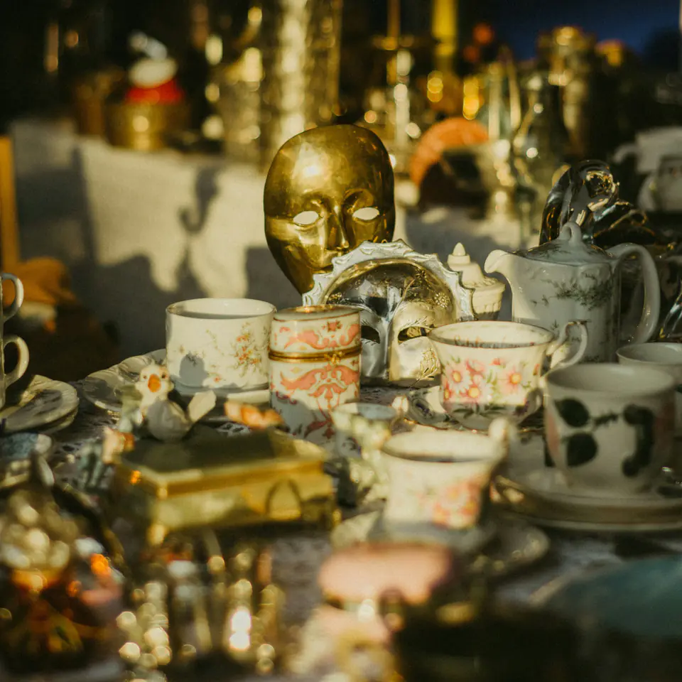 Vintage teacups, a teapot and a gilt mask on a sunlit flea market table in Kyiv