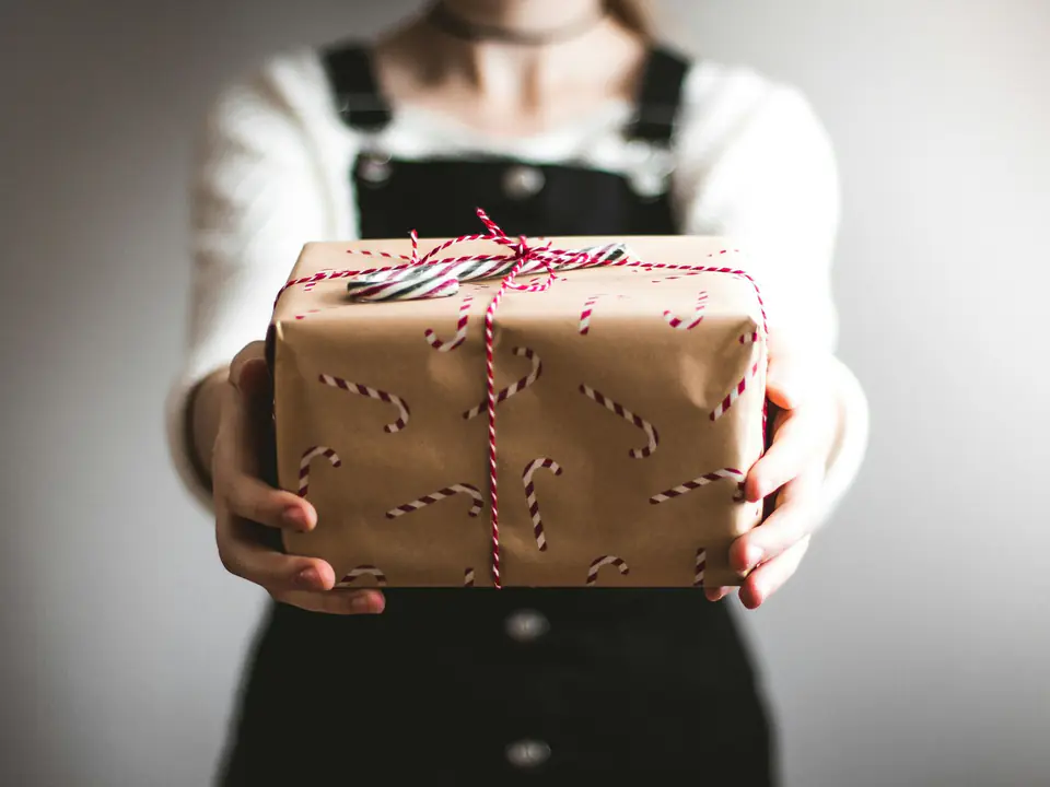 Two hands holding out a present wrapped in brown kraft paper and tied with red-and-white twine