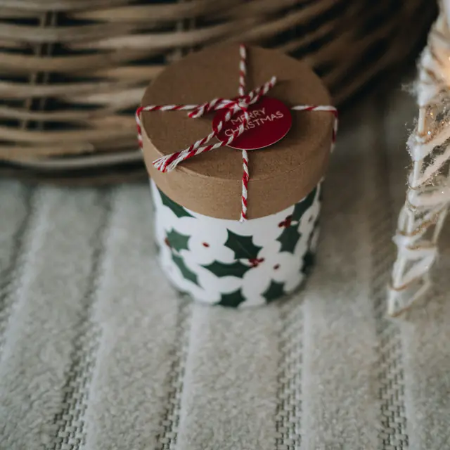 A small holly-patterned gift tin tied with red and white string and a red tag