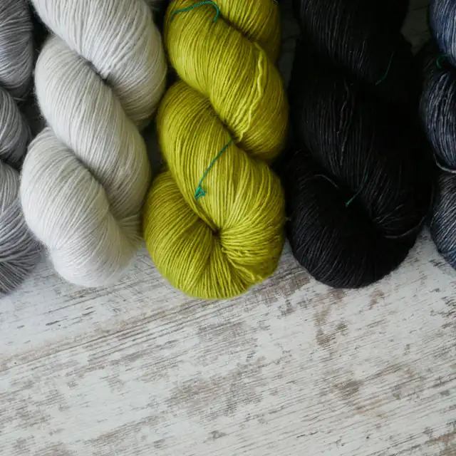 Hand-dyed wool skeins in grey, cream, chartreuse and charcoal on a whitewashed table