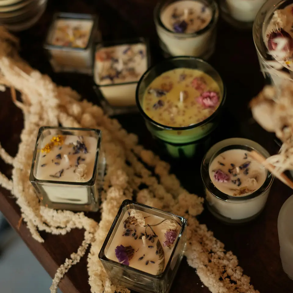 Hand-poured candles with pressed flowers in glass jars on a dark wooden table