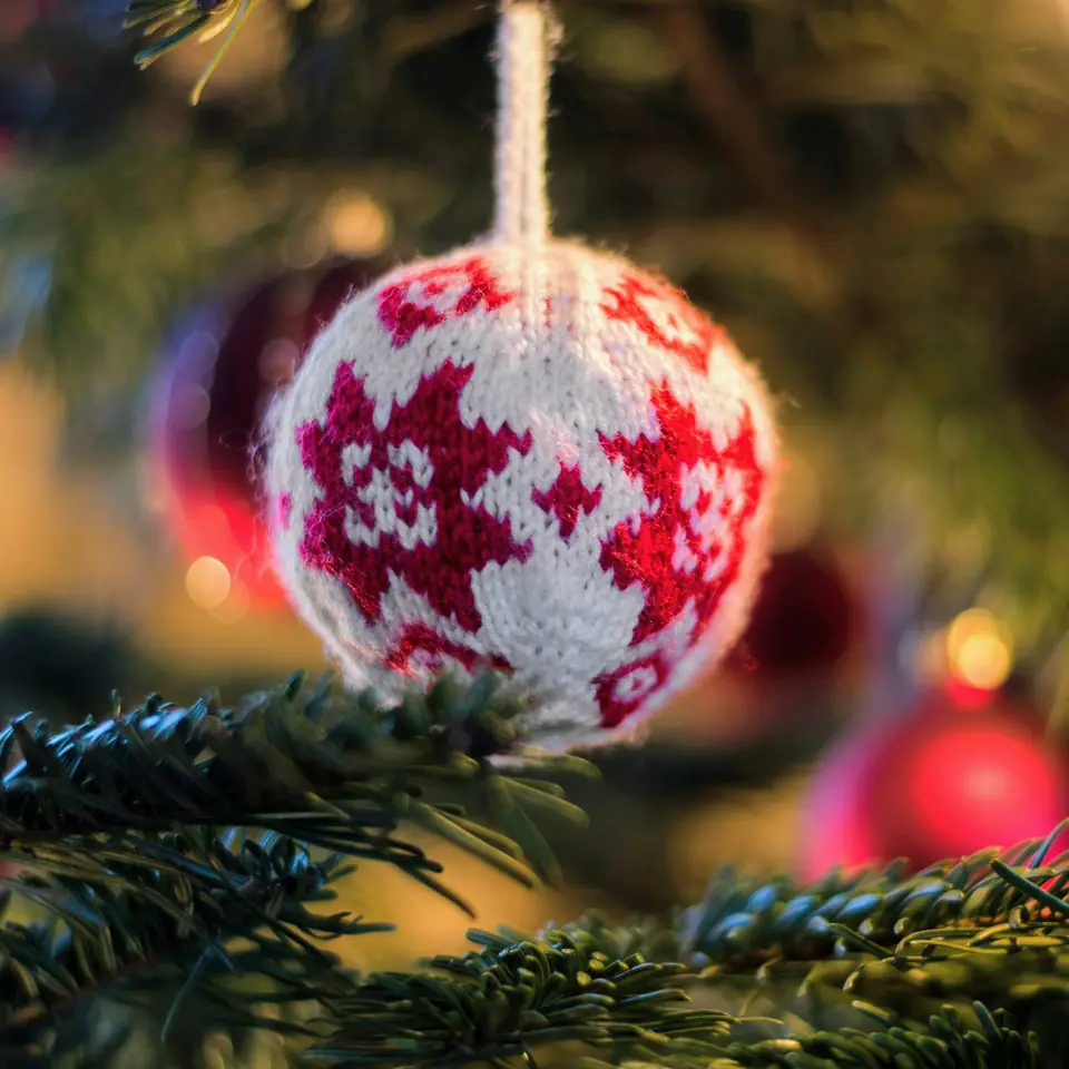 A hand-knit red and white snowflake bauble hanging on a Christmas tree