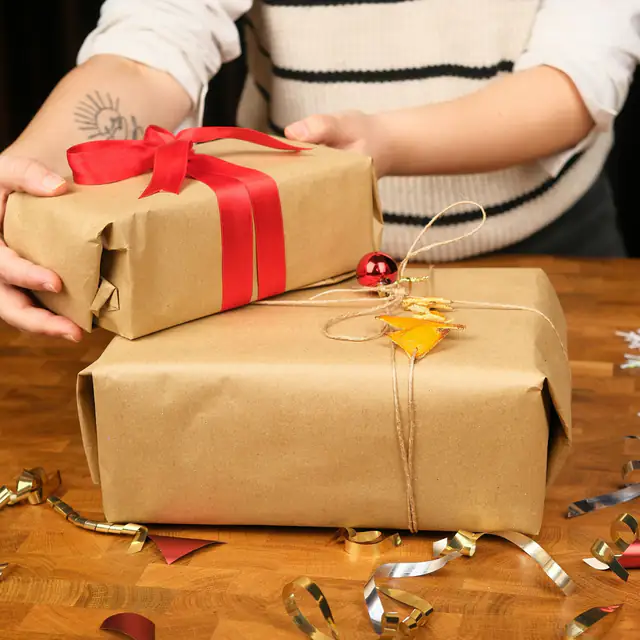 Hands stacking two presents wrapped in kraft paper with red ribbon and twine