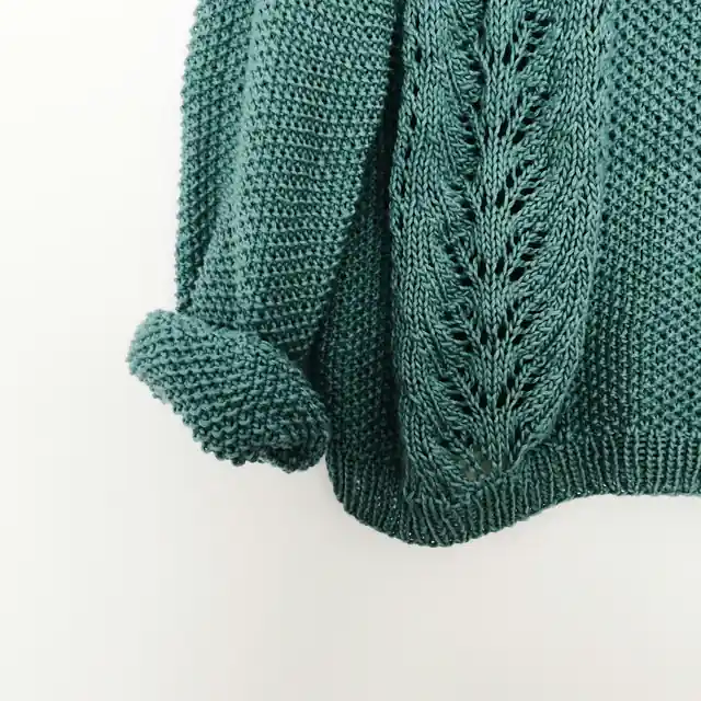 The rolled cuff and leaf-lace front of a hand-knit teal sweater