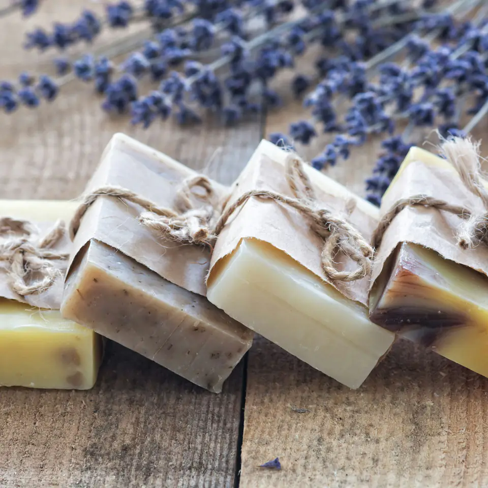 Bars of handmade soap wrapped in paper and twine beside dried lavender on rustic wood