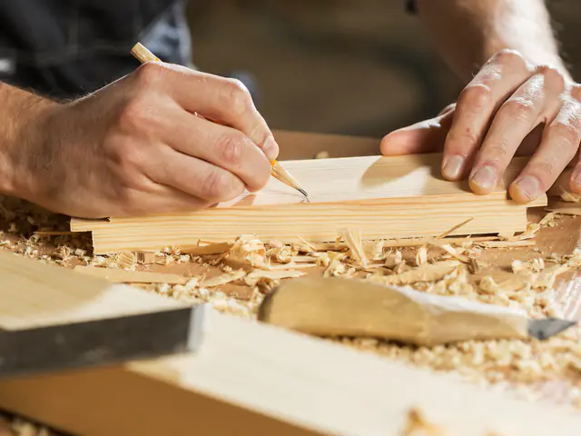 A woodworker’s hands marking a pencil line on a pale pine board among fresh shavings