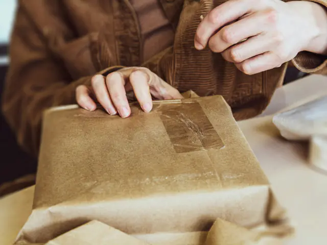 Hands taping brown kraft paper around a parcel on a worktable