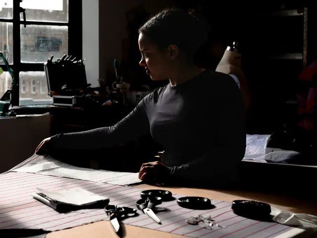 A maker laying out a paper sewing pattern on a large cutting table in a window-lit studio