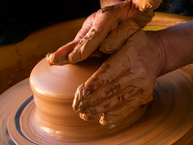 Clay-covered hands shaping a pot on a spinning potter’s wheel