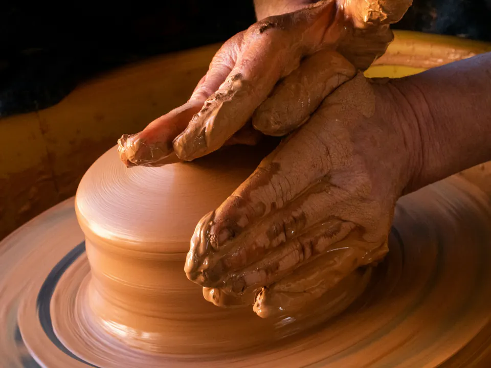 Clay-covered hands shaping a pot on a spinning potter’s wheel