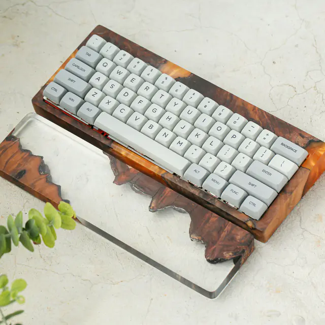 A mechanical keyboard in a handmade walnut and clear resin case, with a matching wrist rest