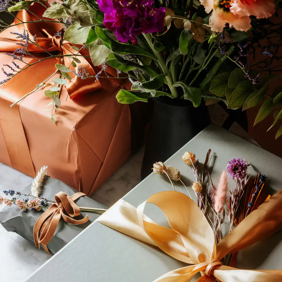 Presents wrapped in copper paper and tied with satin ribbon beside a bunch of fresh flowers