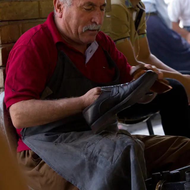 A cobbler in Erbil inspecting a black leather shoe on his lap