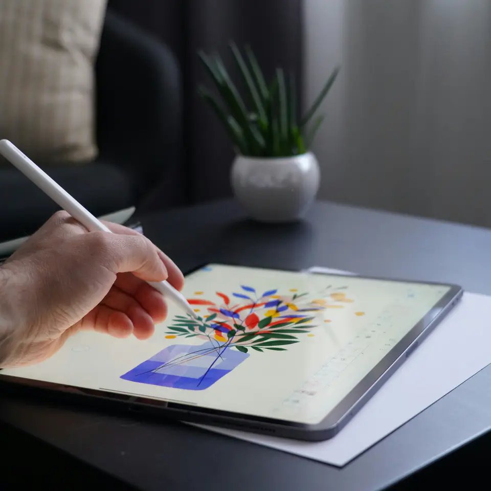 A hand drawing a flower illustration on a tablet with a stylus