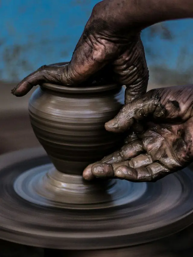 Hands throw a terracotta vase on a spinning pottery wheel in warm light
