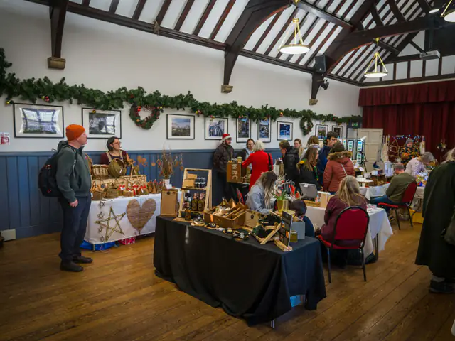 Shoppers browsing tables of handmade goods at a Christmas craft fair in a timber-beamed village hall