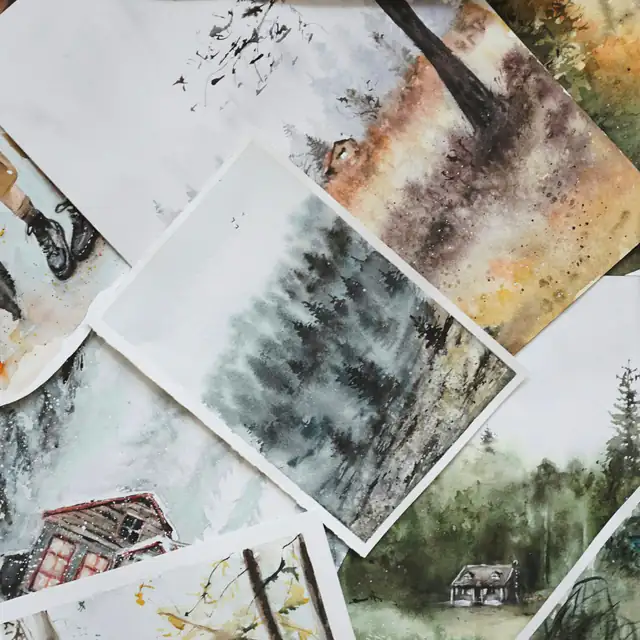 Loose watercolor landscape paintings of forests and cabins spread across a table