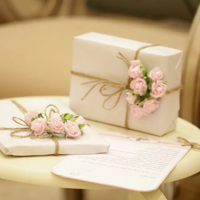 Two gift boxes wrapped in white paper and twine, topped with small pink paper roses