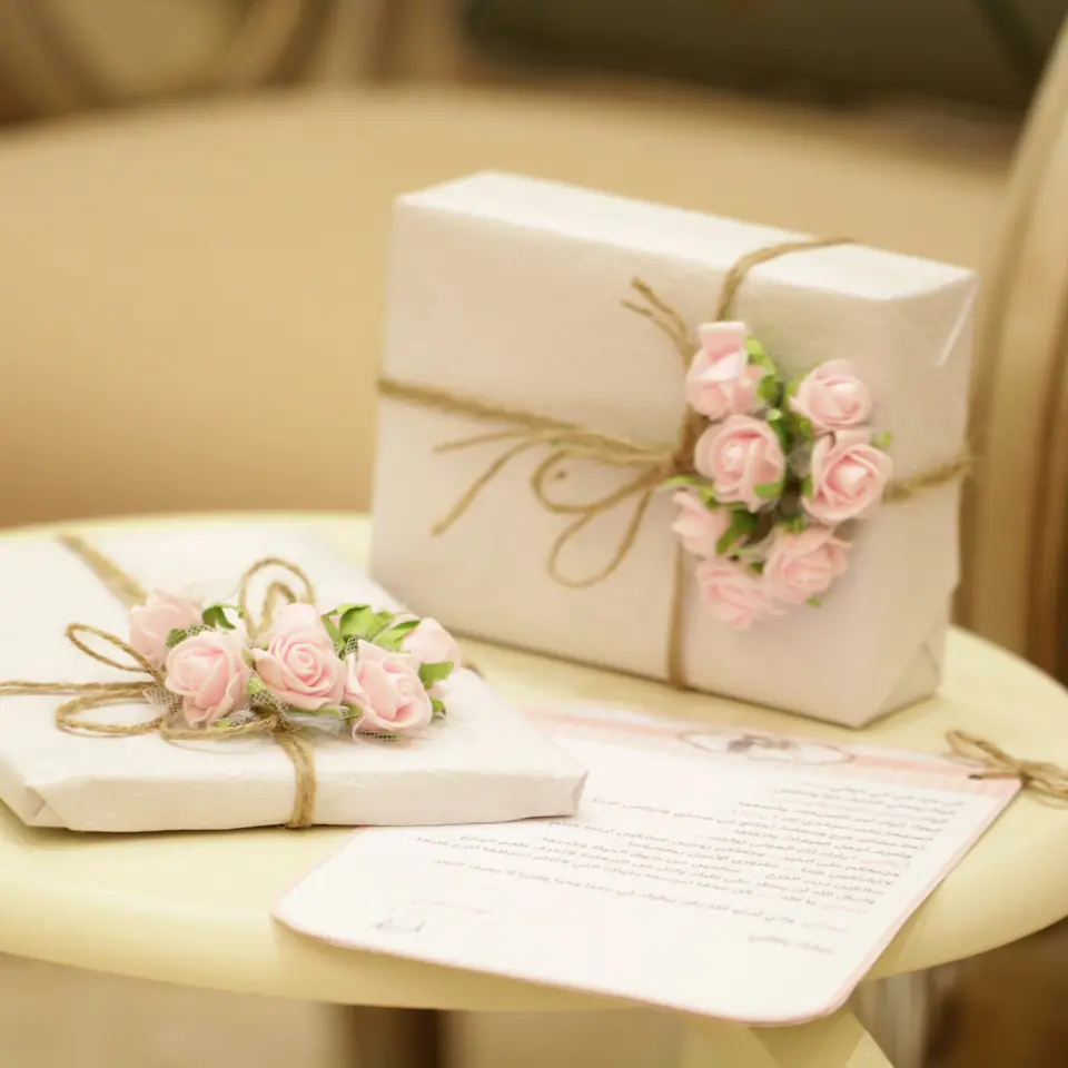 Two gift boxes wrapped in white paper and twine, topped with small pink paper roses