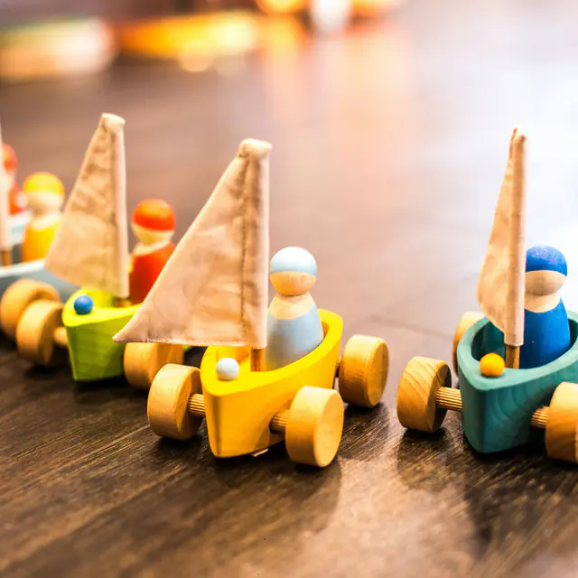Wooden toy sailboats on wheels with peg-doll sailors lined up on a wooden floor