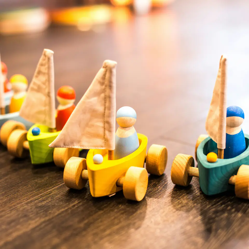 Wooden toy sailboats on wheels with peg-doll sailors lined up on a wooden floor