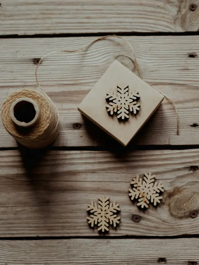 Wooden snowflake ornaments, a kraft-paper box and a spool of twine on rustic wooden boards